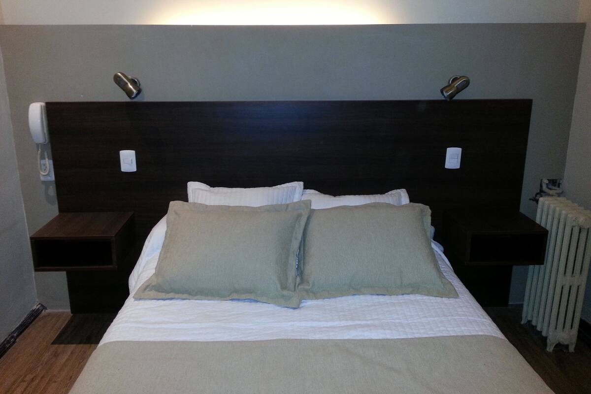Habitación de hotel con una cama grande, dos mesitas de noche, un cabecero y un teléfono instalado en la pared.
