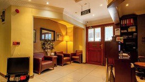 Un vestíbulo de hotel con mostrador de recepción, zona de estar con sillones de cuero, un televisor y una estantería.