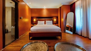Habitación de hotel con una cama grande, lámparas de noche, un espejo y vistas al exterior a través de cortinas.