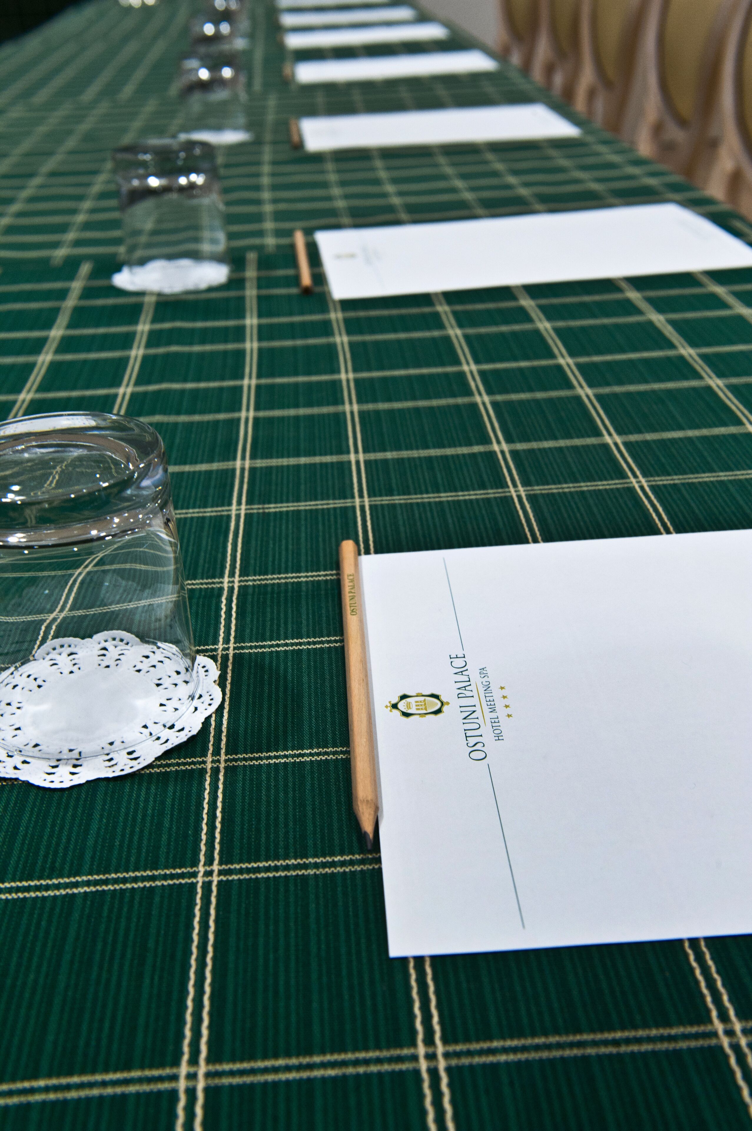 Una mesa con mantel a cuadros verdes, adornada con vasos, un bajo mantel y un menú.