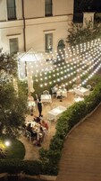 An outdoor dining area with tables and chairs, surrounded by greenery and string lights.