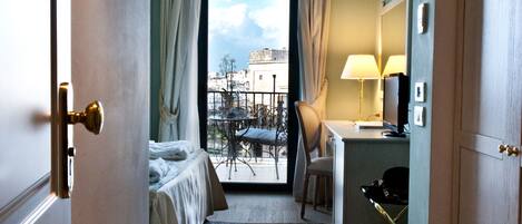 Una habitación de hotel con cama, escritorio con lámpara, silla y vista a la ciudad a través de una ventana.