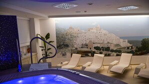 Een wellnessruimte met een jacuzzi, lounge fauteuils en uitzicht op een wit gebouw.