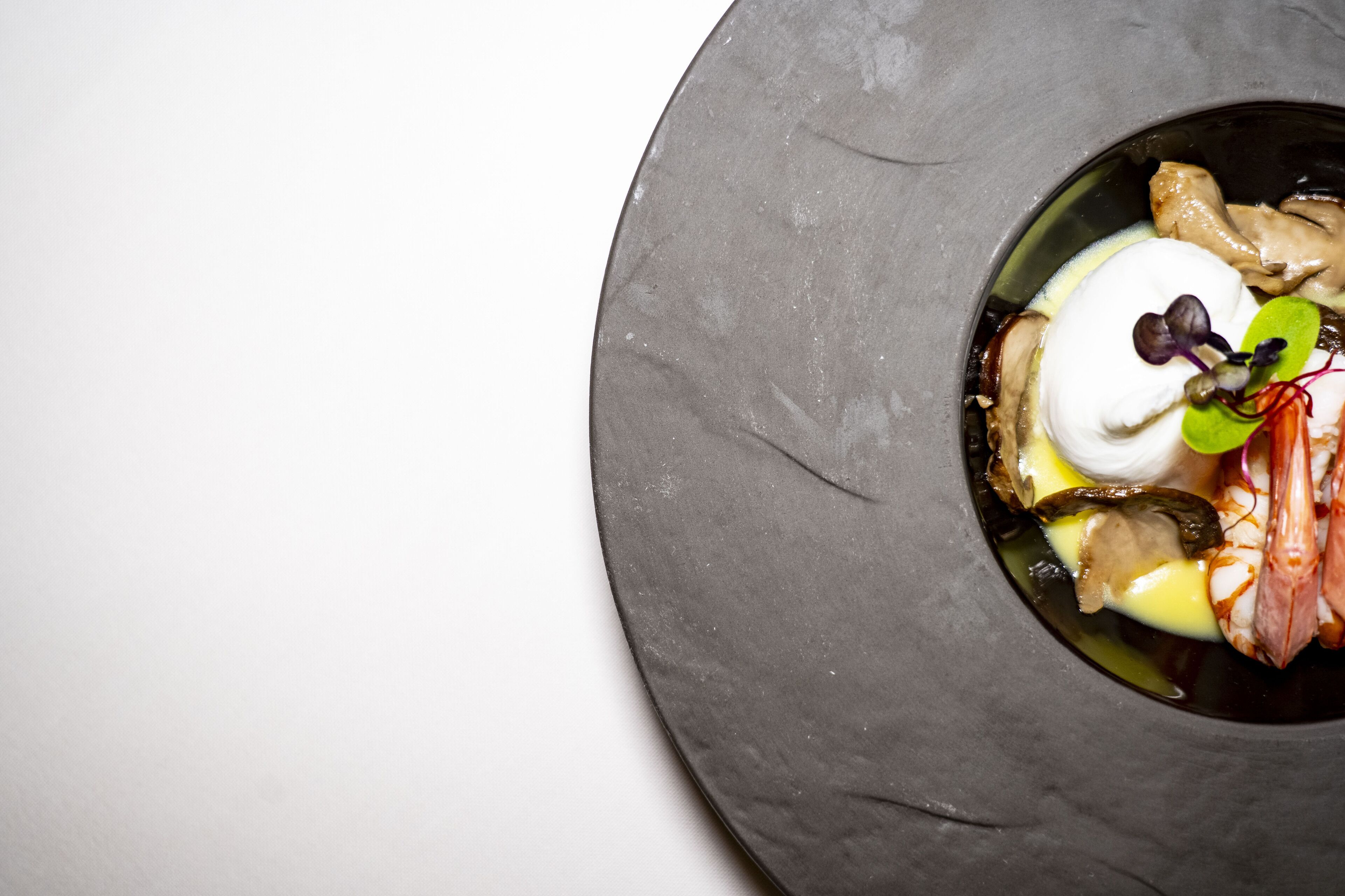 Una mesa redonda y oscura con un plato de mariscos y una cucharada de crema.