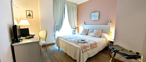 Une chambre d’hôtel bien rangée, avec un lit, une table de chevet, une lampe, une chaise et un petit bureau équipé d’un ordinateur.