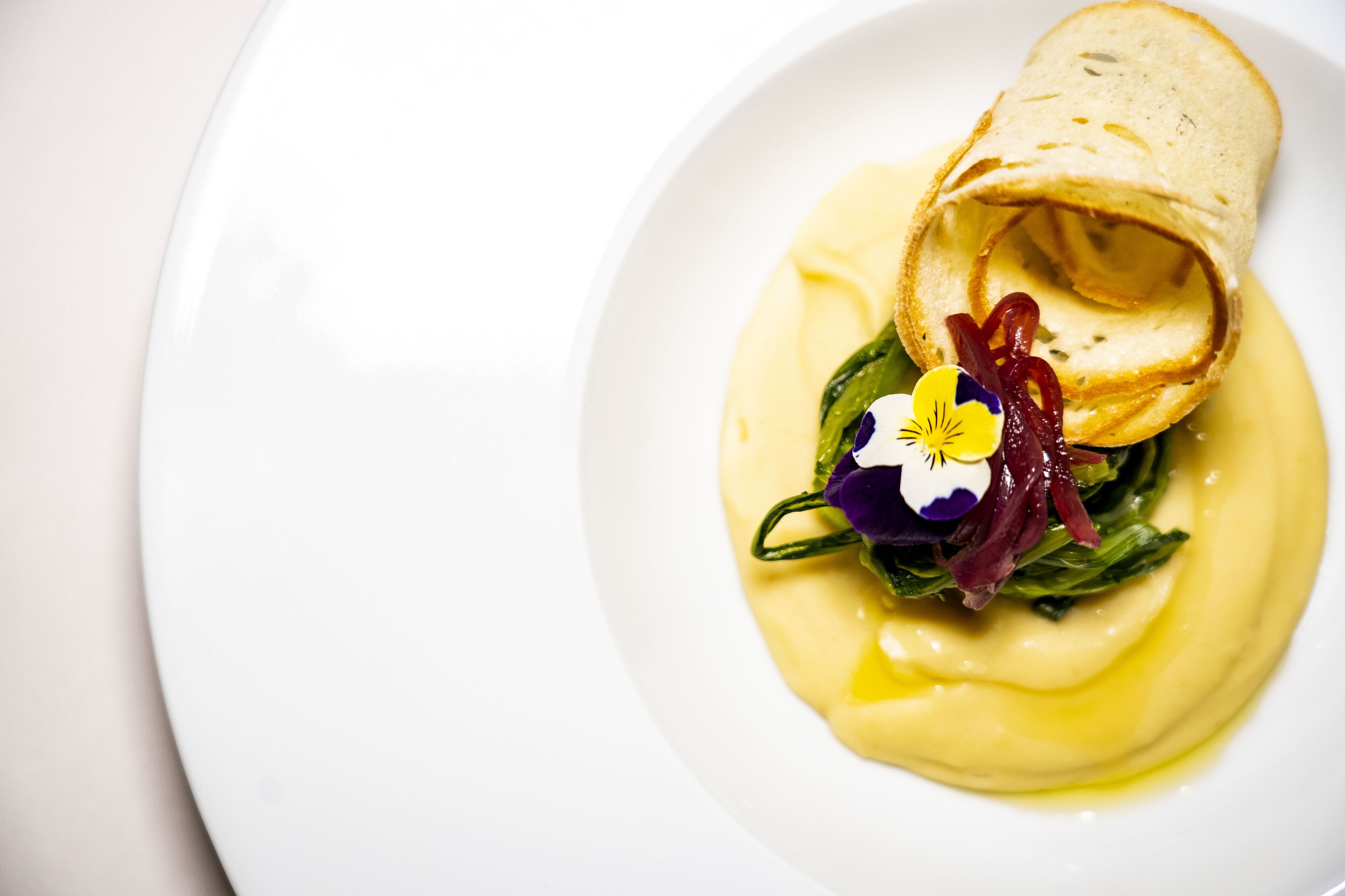 Une assiette contenant une crêpe roulée, des légumes verts et une fleur en guise de décoration.
