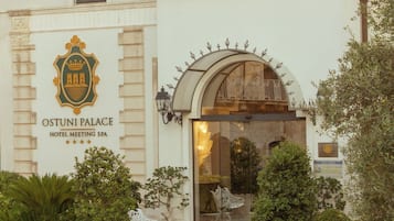 A hotel entrance with a grand archway, a signboard, and a well-maintained garden with potted plants.