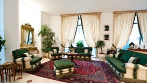 Een ruime woonkamer met een groot rood tapijt, twee groene banken, een salontafel en een decoratieve spiegel.