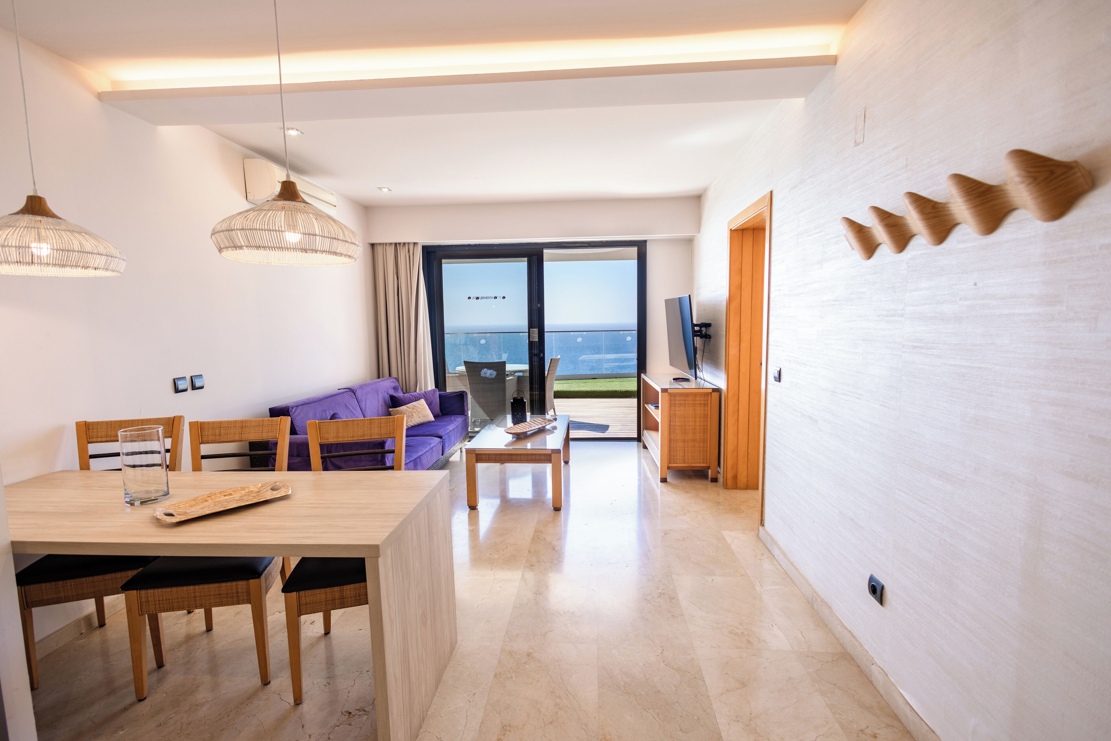 A modern living room with a dining area, large windows, and a view of the sea.