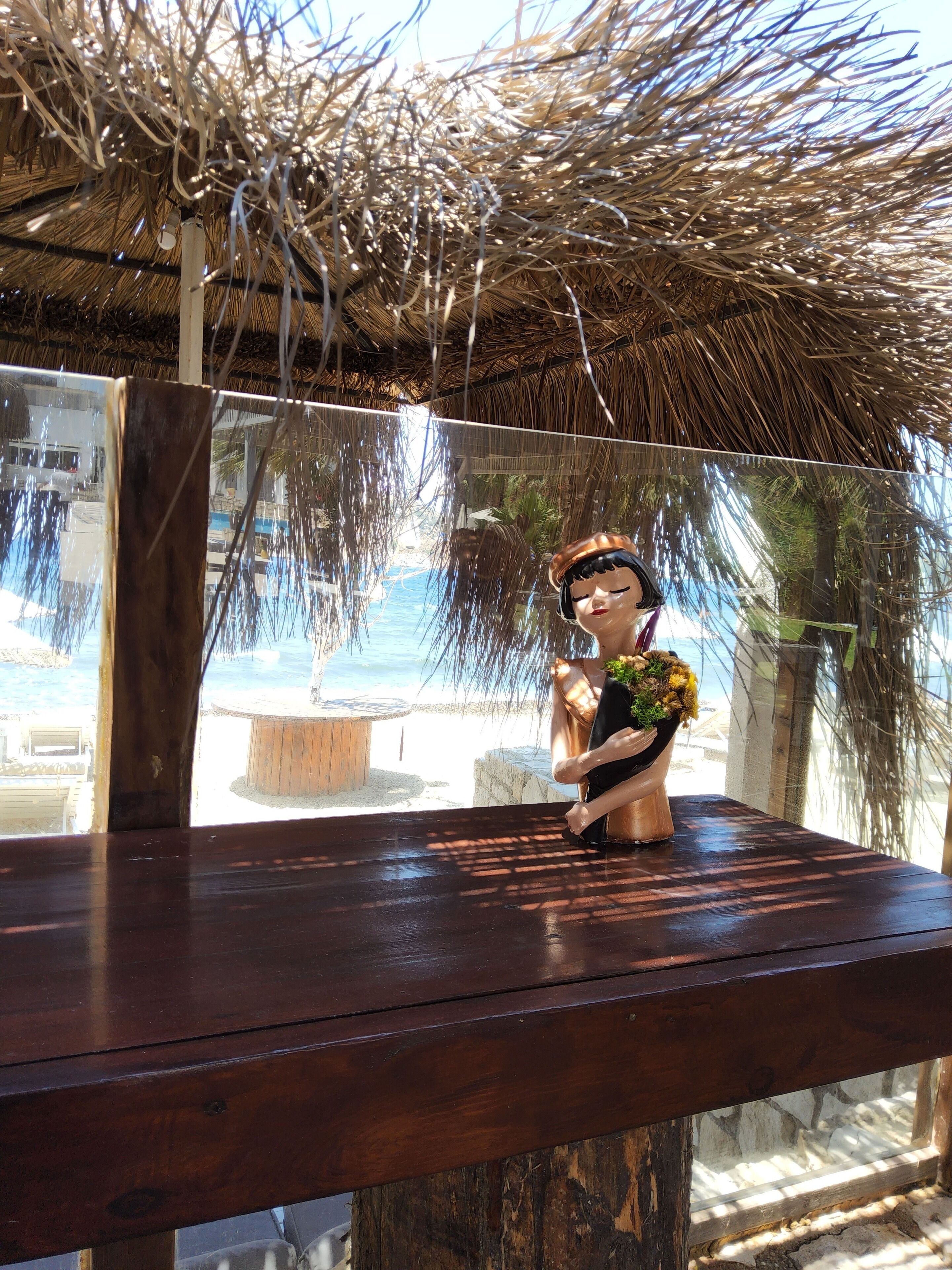 A wooden table with a decorative figure holding a bouquet, under a thatched roof structure.