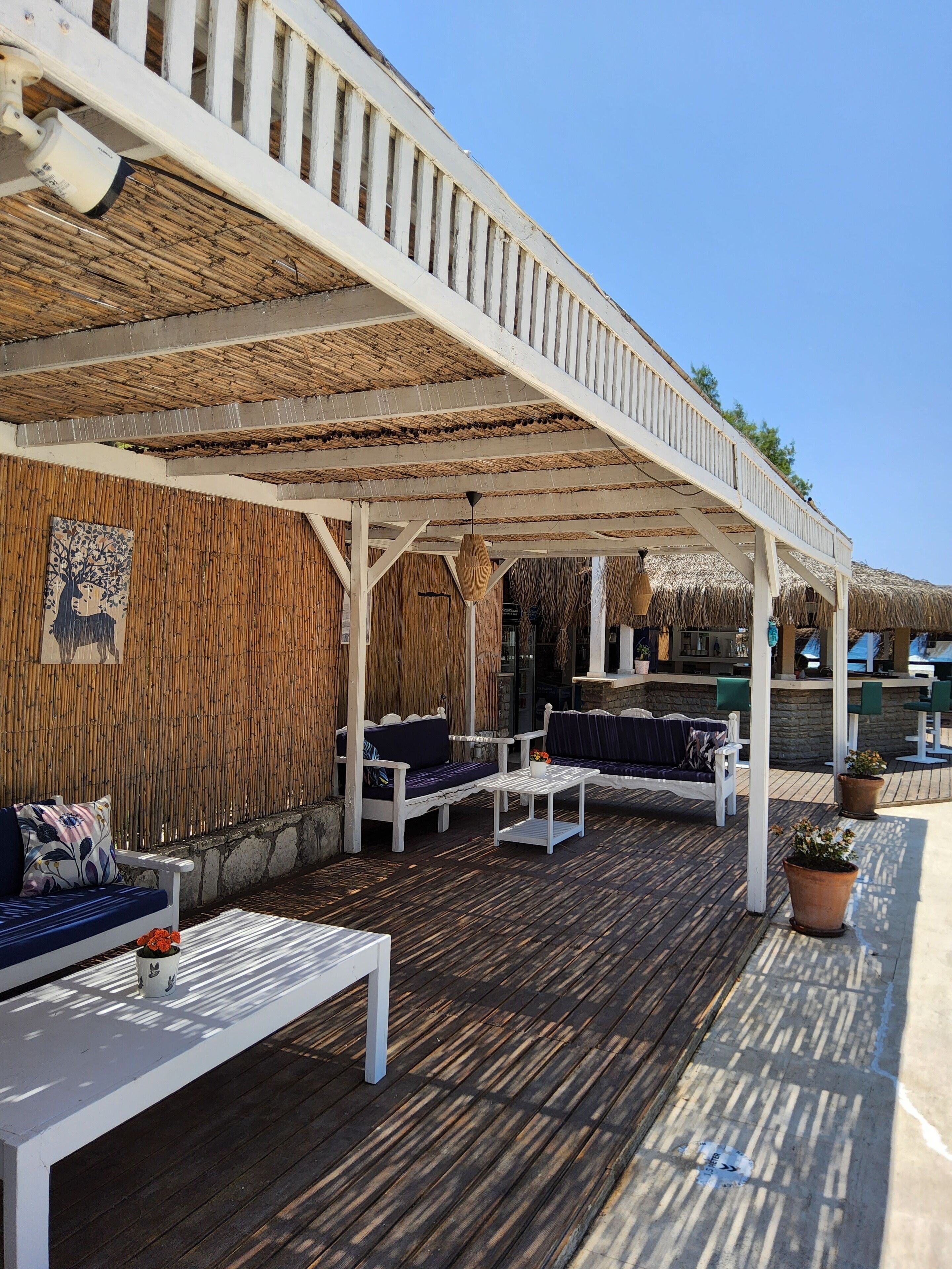 A covered outdoor seating area with white furniture and a thatched roof.