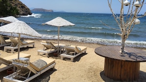 A beach with lounge chairs and umbrellas, a wooden table, and a tree with hanging ornaments. - Ladonia Hotels Zemda Gümüşlük (Bodrum)