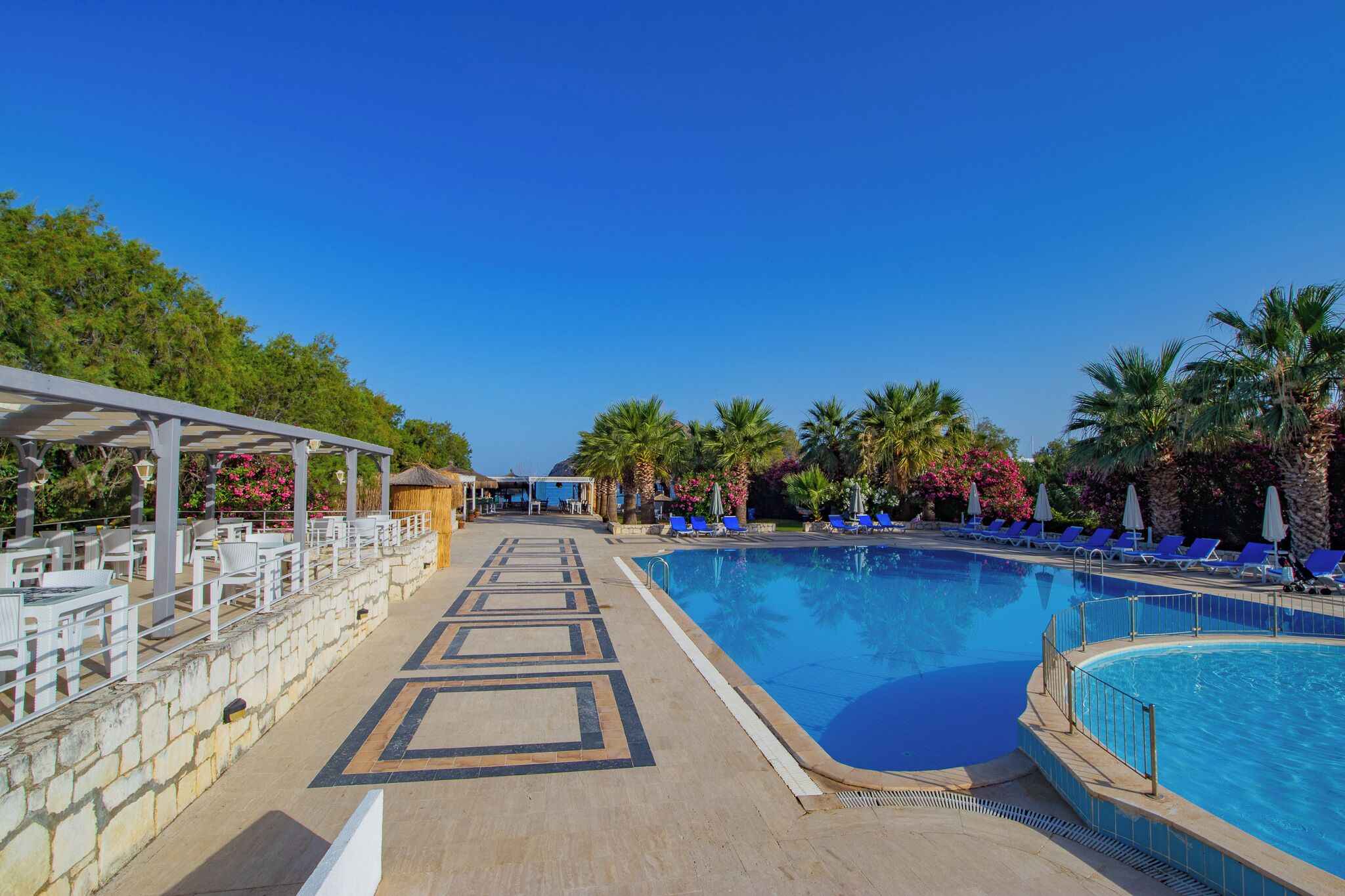 A pool area with lounge chairs, a covered seating area, and a clear blue sky.