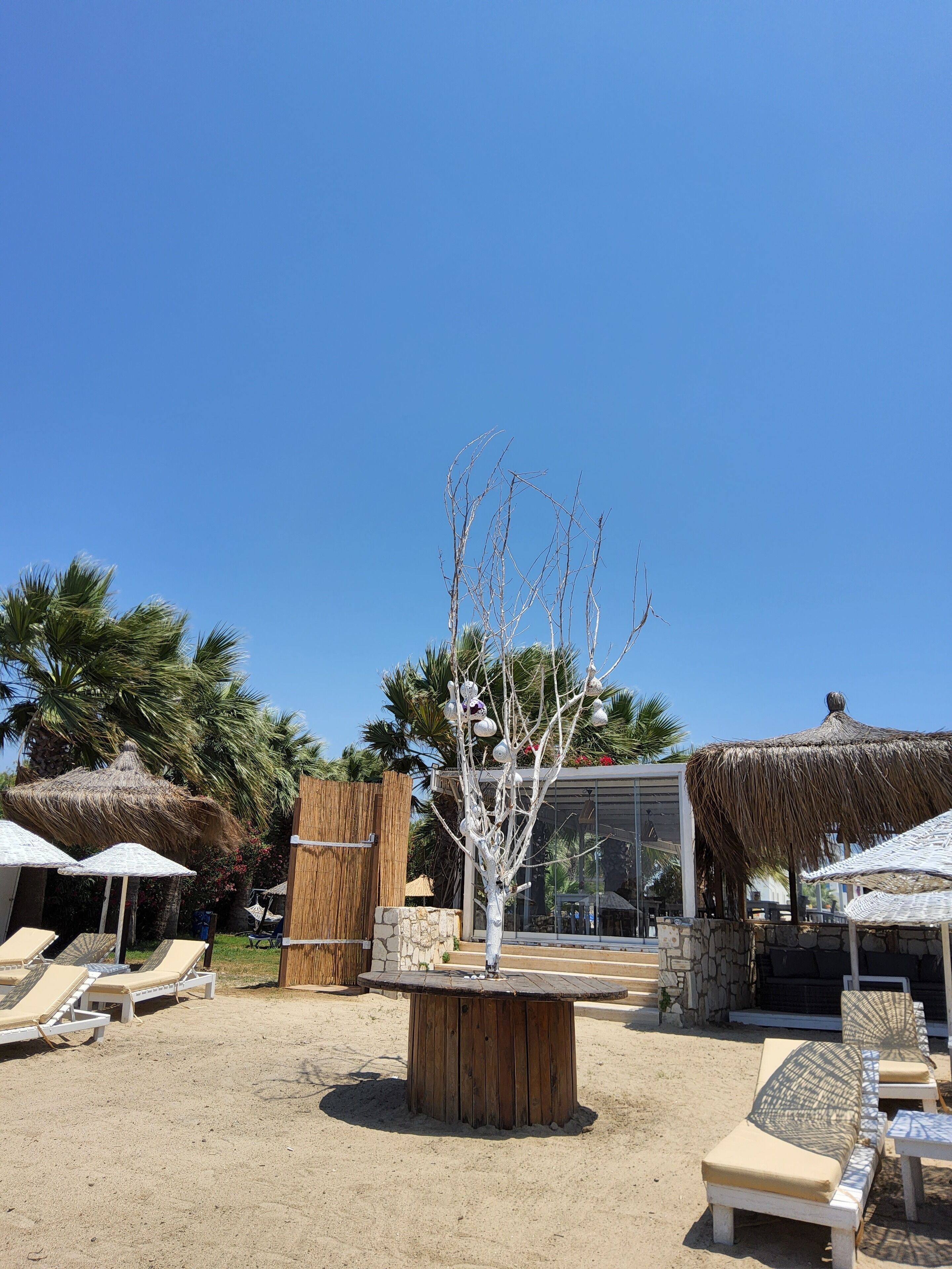 Un área de descanso en la playa con tumbonas, una mesa de madera y sombrillas de paja.