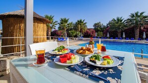 A dining table with plates of food, a glass of red drink, and a poolside setting with chairs and umbrellas. - Ladonia Hotels Zemda Gümüşlük (Bodrum)
