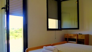 Habitació d'hotel amb un llit, una taula de treball, un mirall i una finestra amb persianes.