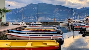 A marina with various boats docked, a mountainous backdrop, and a calm water surface reflecting the boats. - Hotel Merano (Brenzone sul Garda)
