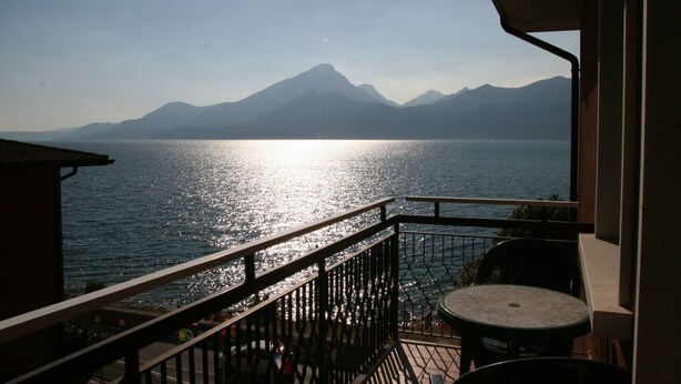 A balcony with a view of a calm sea and distant mountains. - Hotel Merano (Brenzone sul Garda)