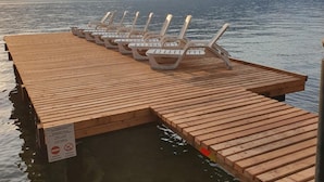 A wooden dock with lounge chairs extending over a body of water, with mountains in the background. - Hotel Merano (Brenzone sul Garda)