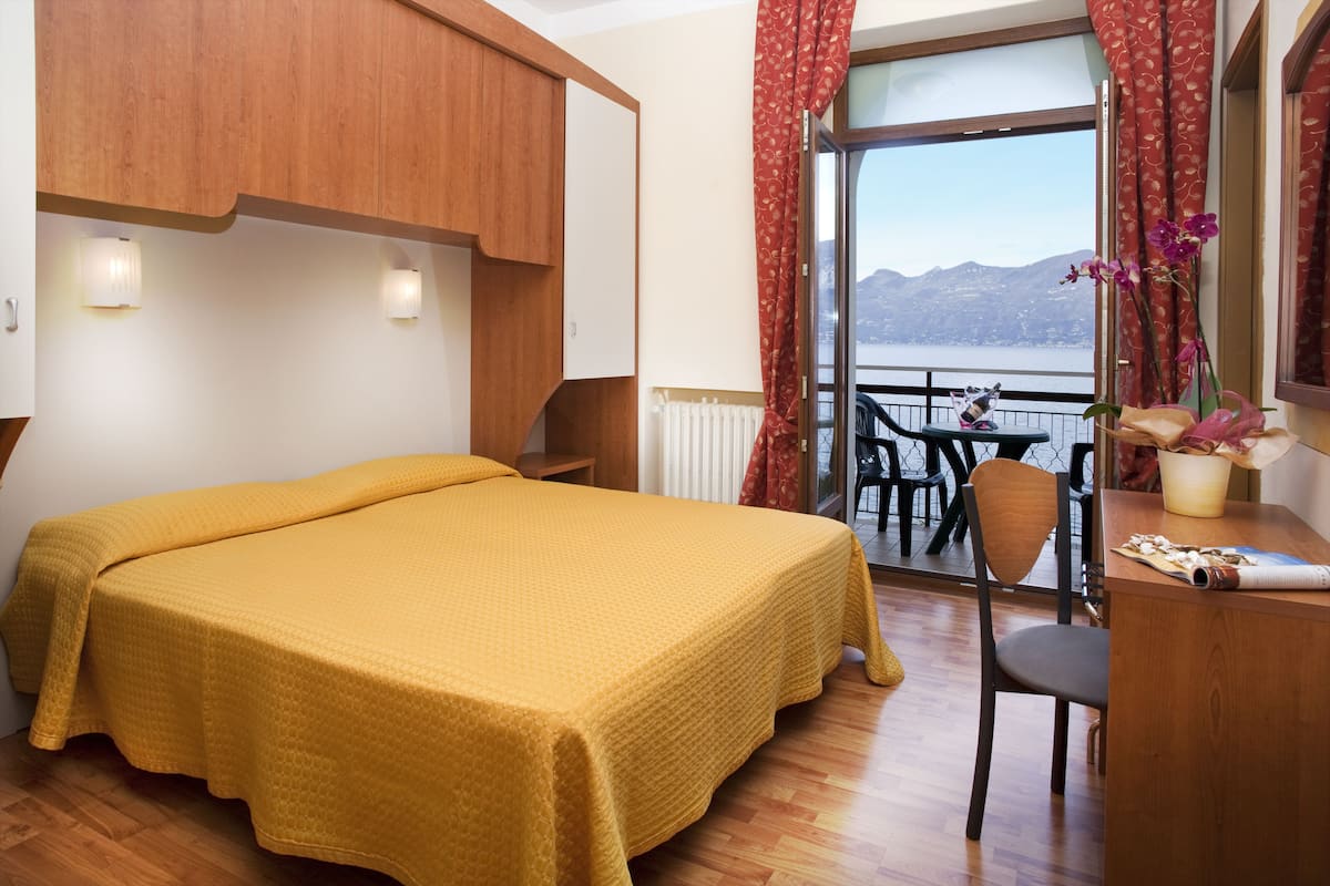 A room with a bed, a desk, a chair, and a view of a lake through a window.