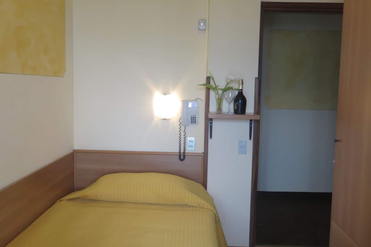 A hotel room with a bed, a bedside table, a phone, a mirror, and a door.