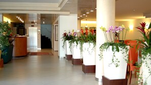 A hotel lobby with a reception desk, a staircase, and potted plants. - Hotel Capri (Bardolino)