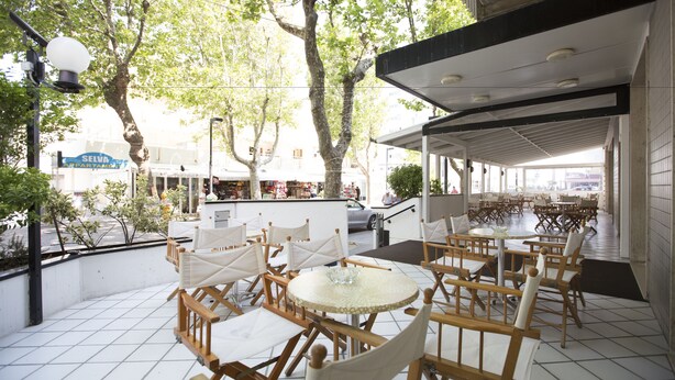Un café al aire libre con mesas y sillas, una zona de estar cubierta y vistas a la calle.