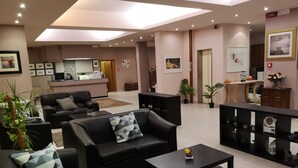 Una sala de estar moderna con sofás de cuero negro, una mesa de centro y un área de recepción con mostrador y cuadros enmarcados.