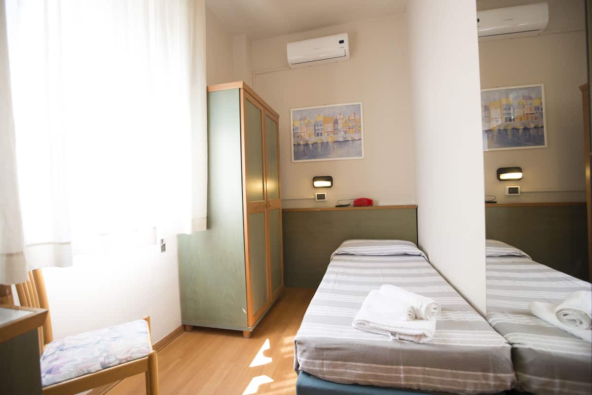 A hotel room with a bed, a desk, a chair, a wardrobe, and a mirror.