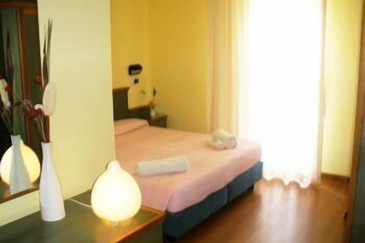 A hotel room with a bed, bedside table, lamp, and a mirror.