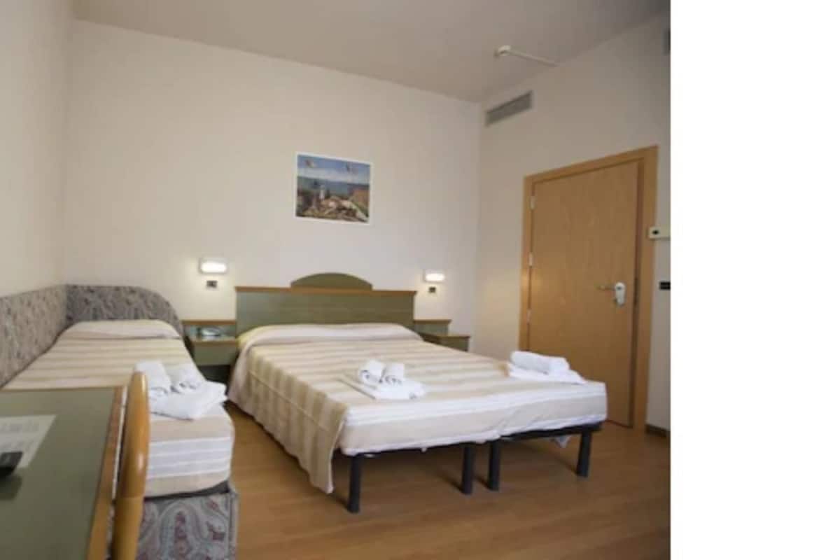 A hotel room with two single beds, a small desk, and a chair.