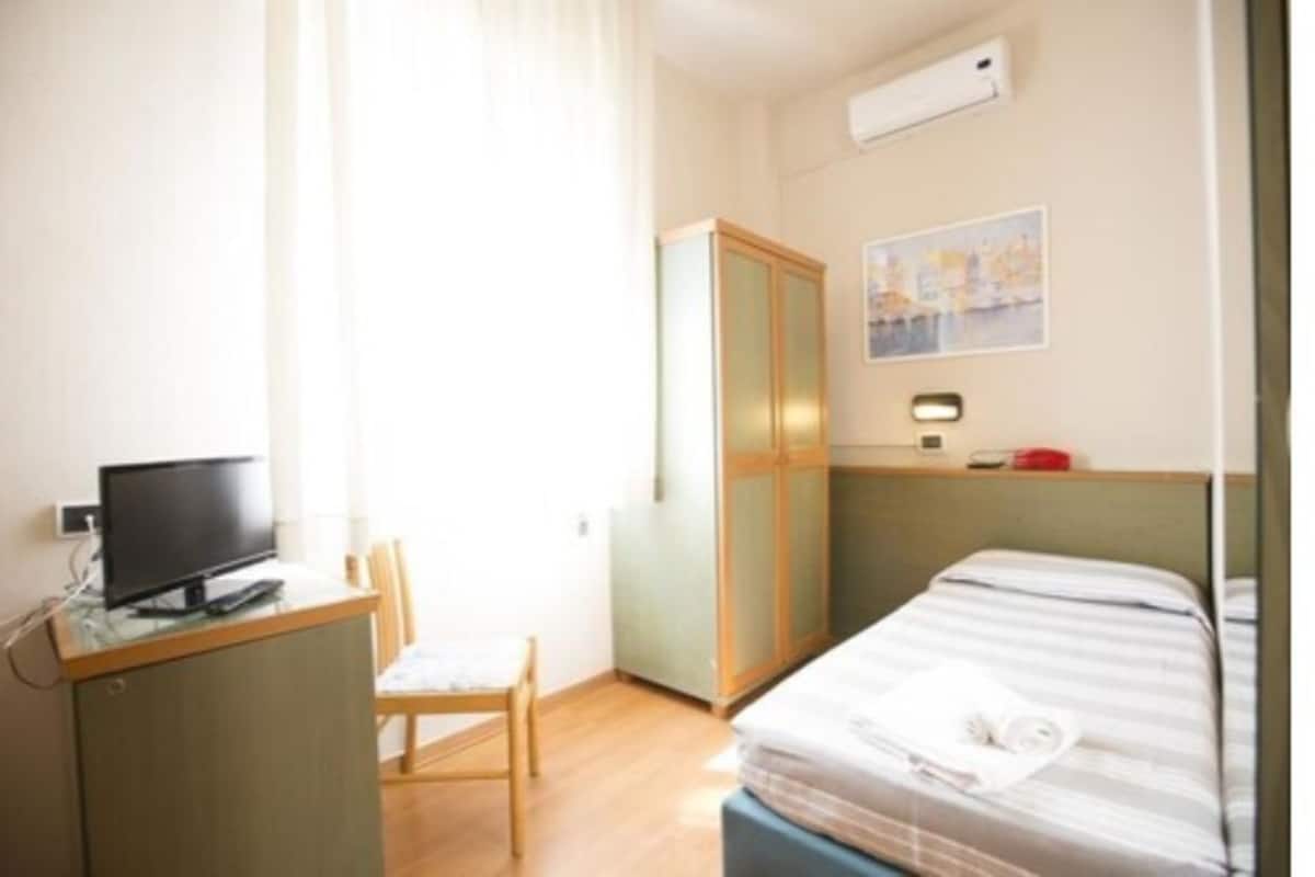 A hotel room with a bed, a desk with a computer, a chair, and a wardrobe.