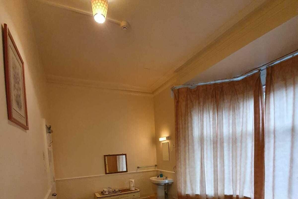Habitación de hotel con una cama grande, una mesita de noche, un espejo, una ventana con cortinas y una lámpara en el techo.