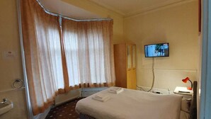 A hotel room with a bed, a television, a small table with a tray of food, a sink, and curtains. - The Handforth Lodge (Wilmslow)