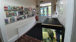 A hallway with a wall of postcards, a fire exit sign, a radiator, and a fish tank. - The Handforth Lodge (Wilmslow)