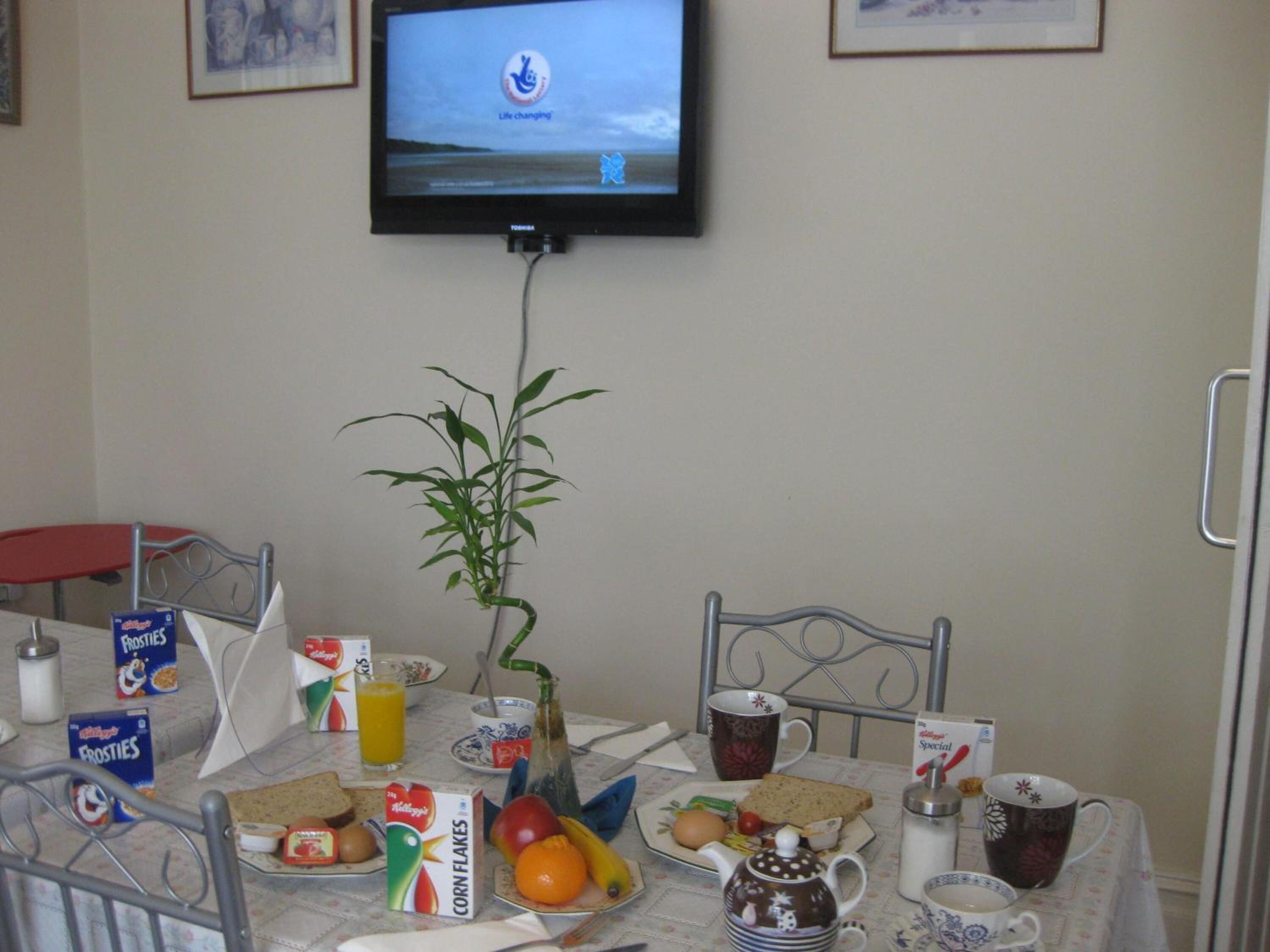 Ein Frühstückstisch mit Müsli, Früchten, einem Teekessel und einem Fernseher, der ein Logo zeigt.