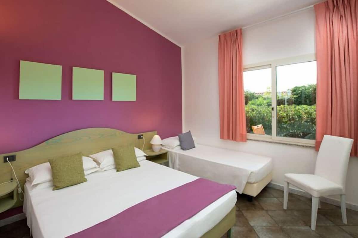 A hotel room with a large bed, a smaller bed, a chair, and a window with curtains.