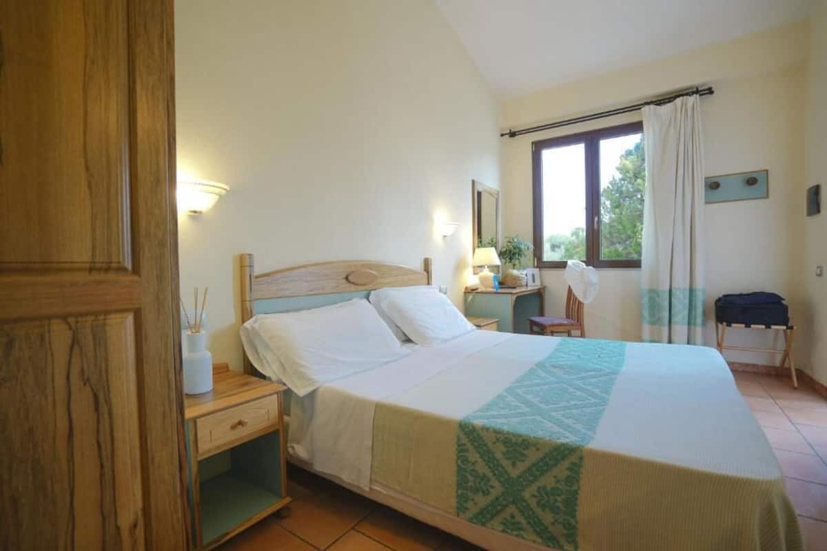 A bedroom with a bed, bedside table, lamp, and a window with curtains.