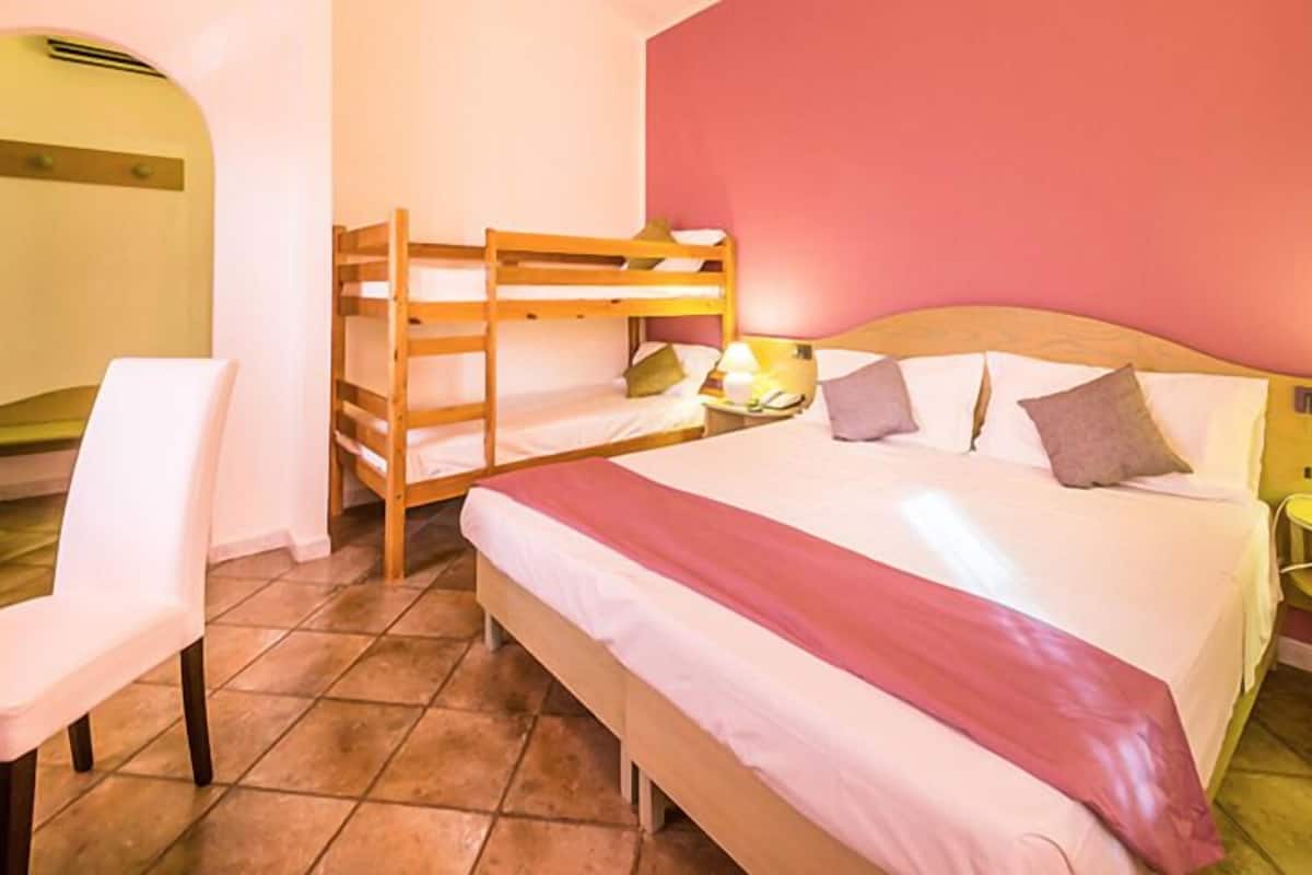 A bedroom with a bunk bed, a single bed, a chair, and a bedside table with a lamp.