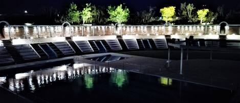 A swimming pool with steps leading into it, surrounded by a stone wall and trees.