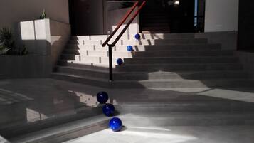A modern building with a staircase, a glass railing, and a few blue spherical objects on the ground.