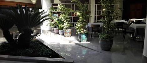 Un espacio interior amplio con piso pulido, varias plantas en macetas y mesas dispuestas para comer.