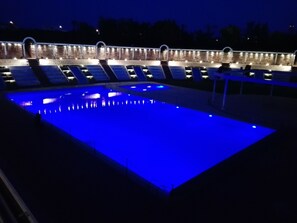 A swimming pool with a blue-lit bottom, surrounded by a covered area with seating and a brick wall. - D'Aragona Lifestyle Hotel (Conversano)