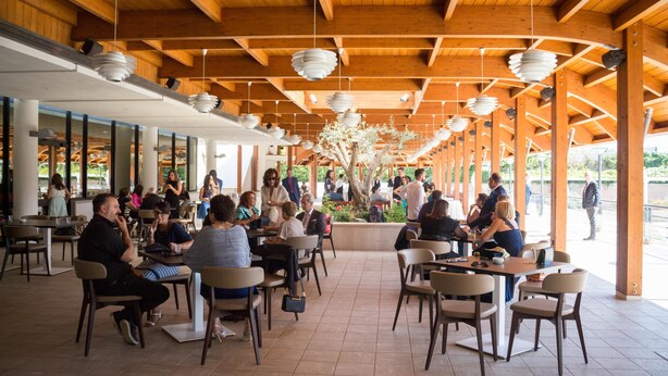 Un café en plein air avec des poutres en bois et des lampes suspendues, entouré de tables et de chaises.