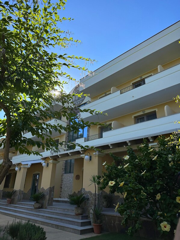 A multi-story hotel with balconies, a stone facade, and potted plants. - Hotel Cala dei Pini (Sant'Anna Arresi)