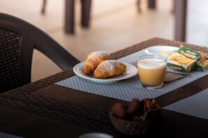 A table with croissants, a glass of coffee, and a box of cereal. - Hotel Cala dei Pini (Sant'Anna Arresi)