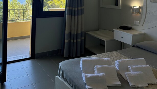 Quarto de hotel com cama, mesa de cabeceira, espelho e vista para o exterior.