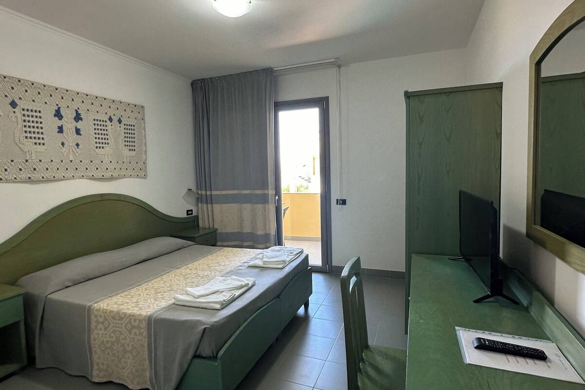 Une chambre d’hôtel avec un lit, un bureau et une chaise, une télévision et une fenêtre avec des rideaux.