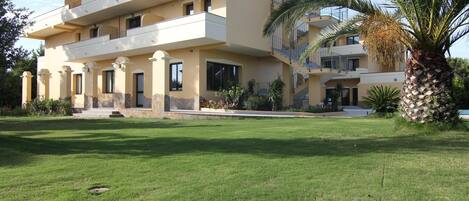 A multi-story building with balconies, a well-maintained lawn, and palm trees.
