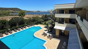 Uma piscina com design sinuoso, rodeada por espreguiçadeiras e vista para o mar.
